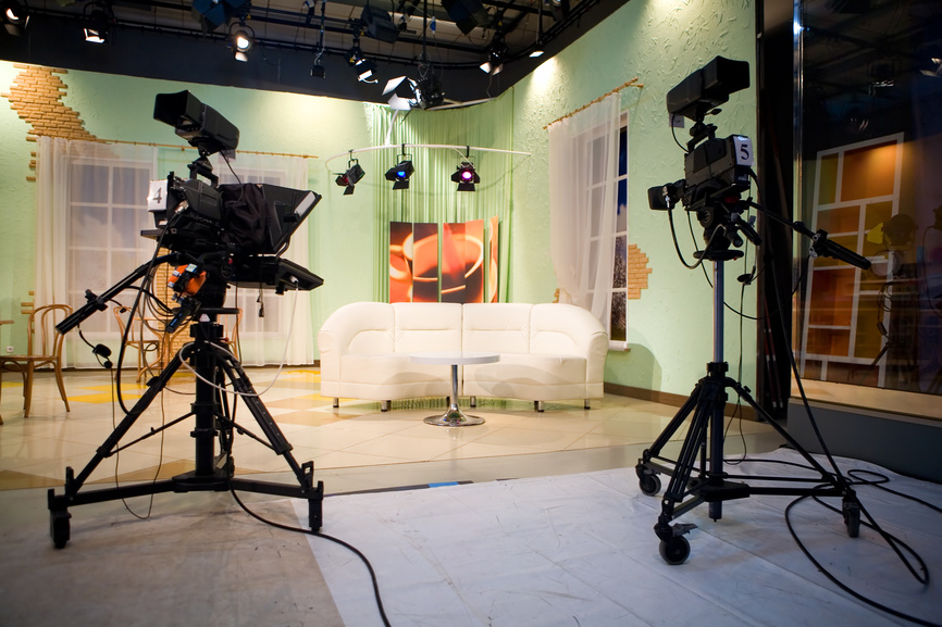 Bild eines ausgeleuchteten Studios mit zwei Kameras und einer weißen Couch in der Mitte