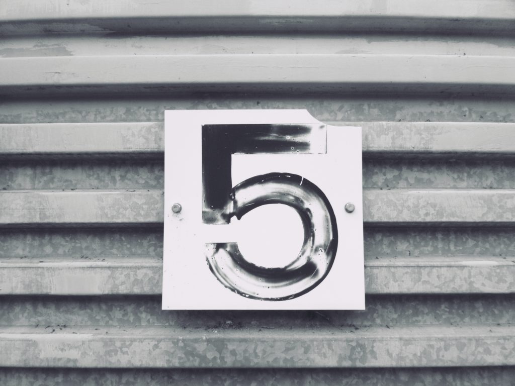 Die Zahl 5 in schwarzer Farbe, dass auf einem weißen Schild an Wellblech befestigt ist