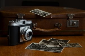 Alte Fotografien und eine alte Kamera stehen auf einer Holzoberfläche vor einem alten Koffer